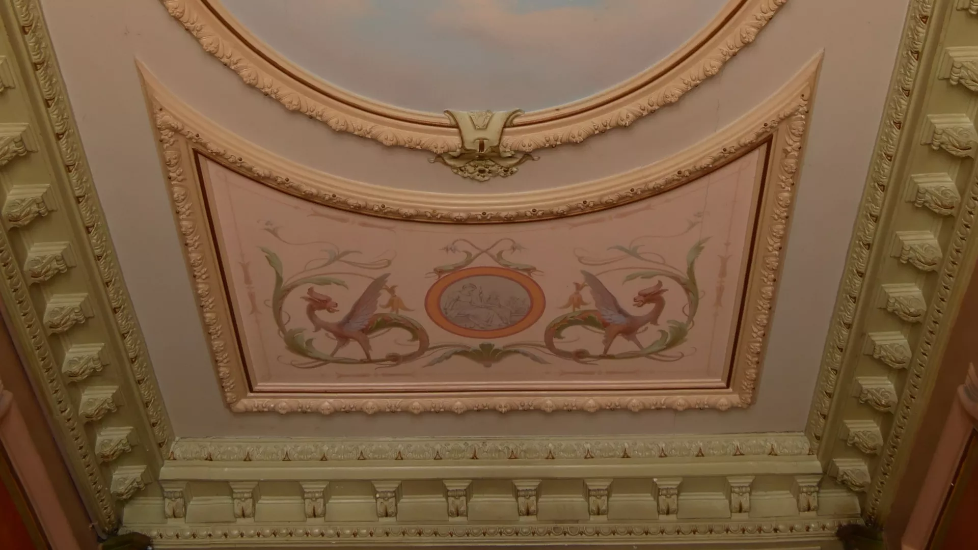 Détail d'un plafond de cage d'escalier avec moulures et décor peint comportant un dragon stylisé dans un rinceau