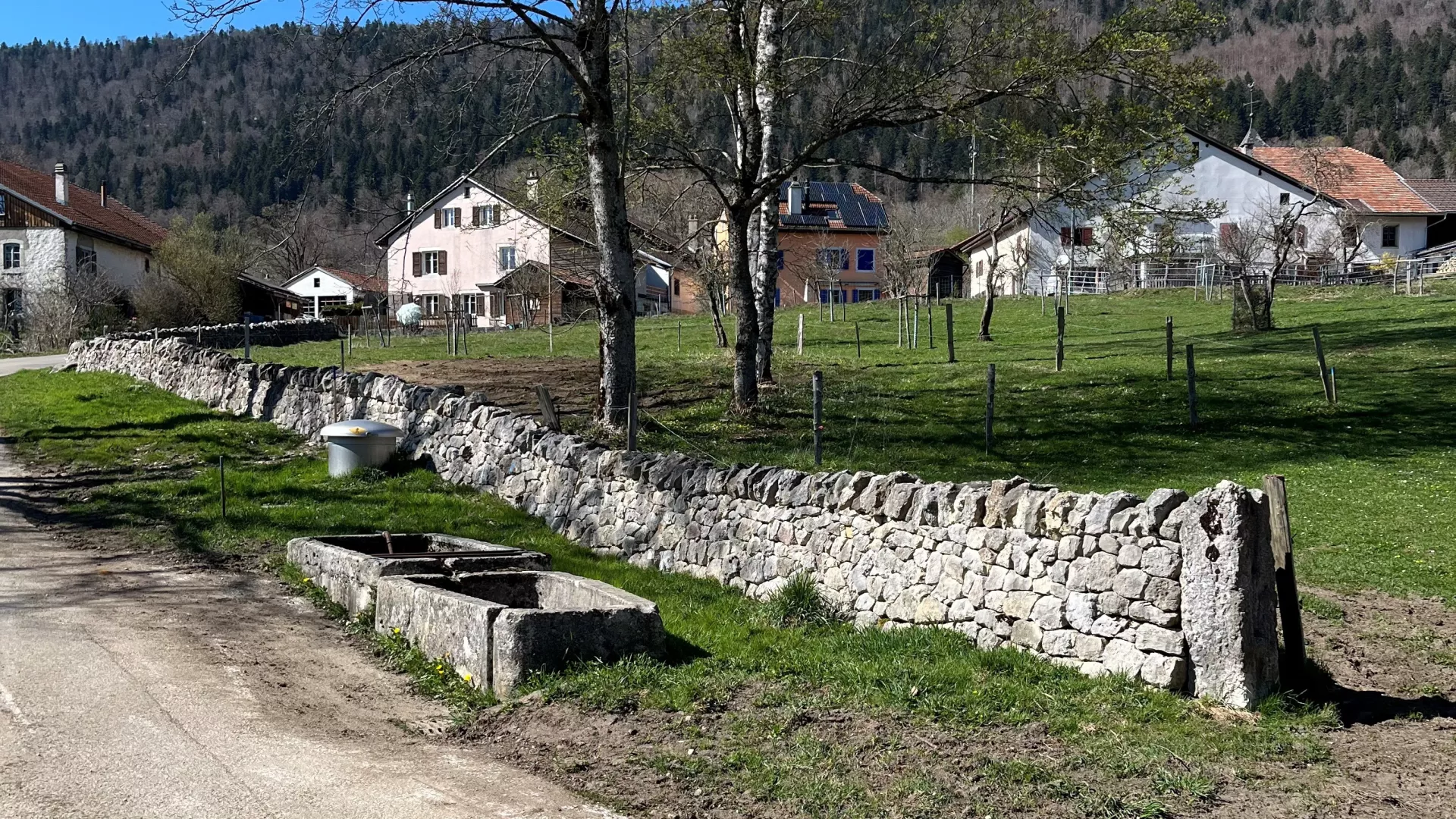 Mur en pierres sèches avec des fermes jurassiennes en arrière-plan